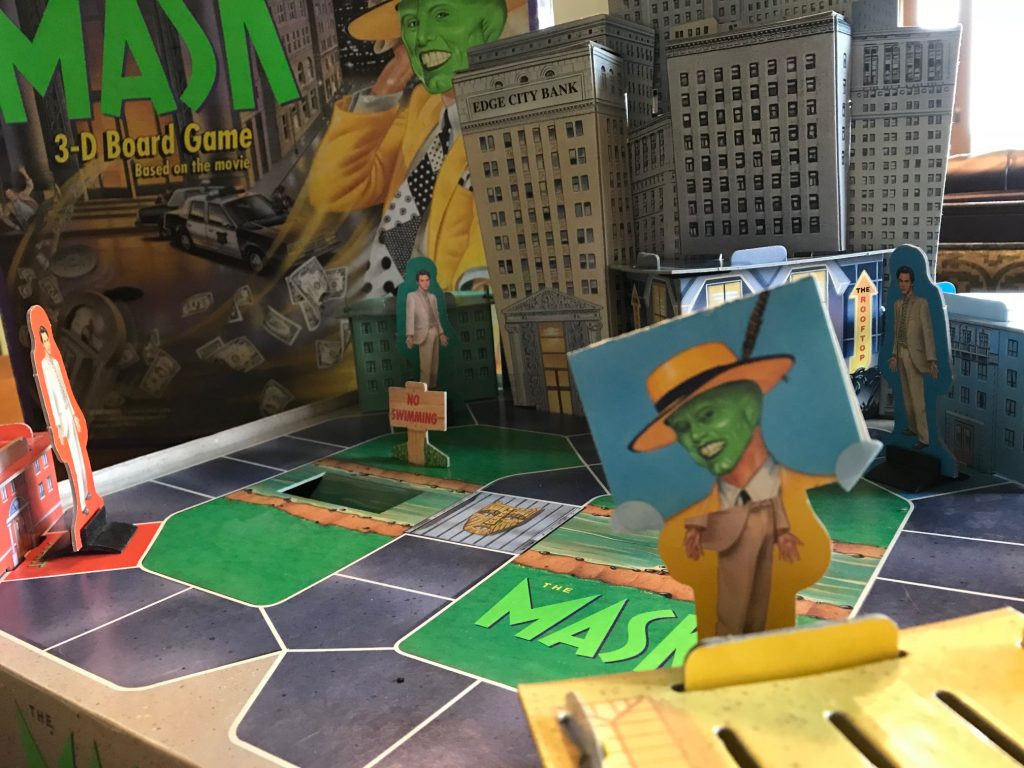 The board showing 3-d buildings and Stanley pawns, one wearing a mask