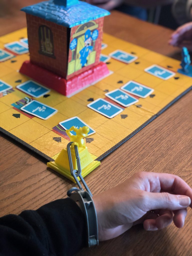 One hand handcuffed to corner of the board and all the cards are in place