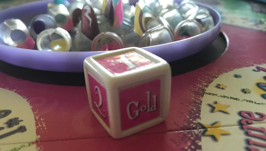 The pink die showing numbers and the word Gold on one side