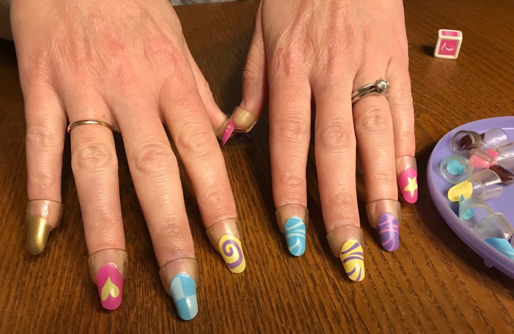 Two hands showing one gold nail and 9 funky fingernails